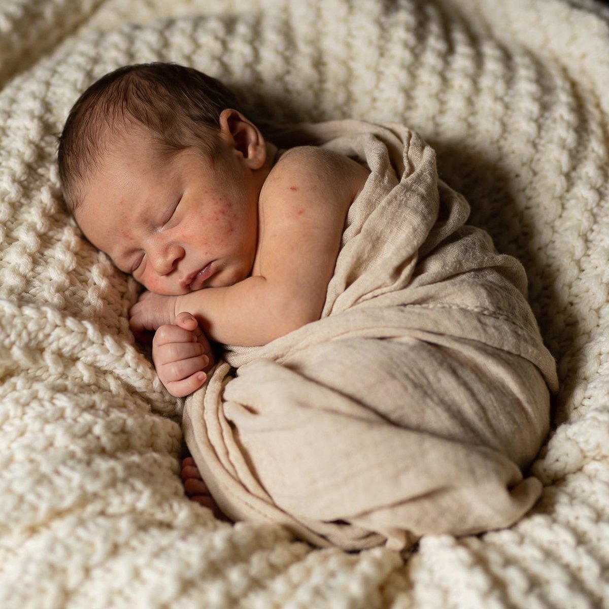 Newborn baby in a sculpted curled pose inside a knitted basket, photographed within the first two weeks of life