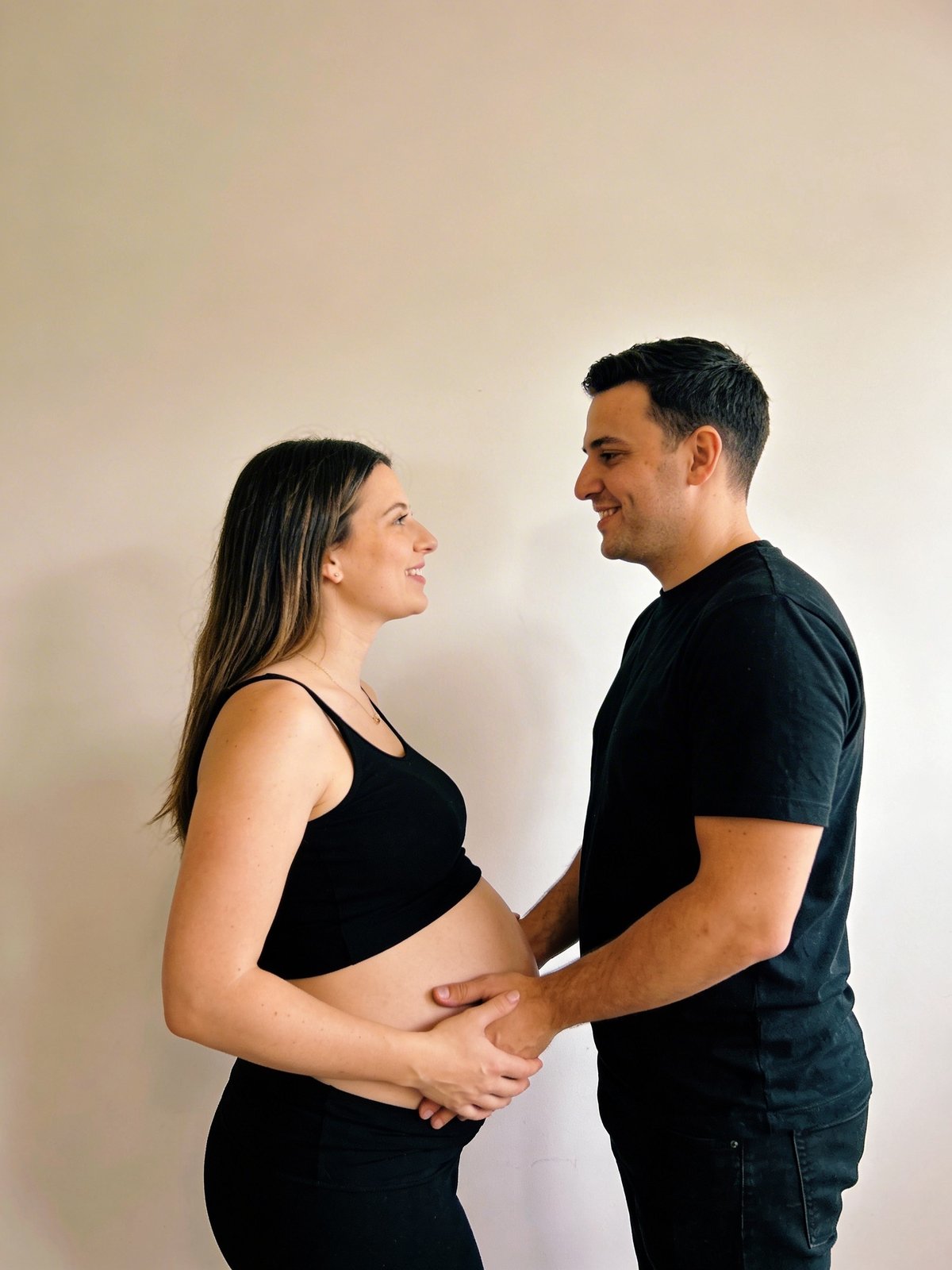 Expecting couple in coordinated neutral outfits outdoors, hands gently resting on the bump